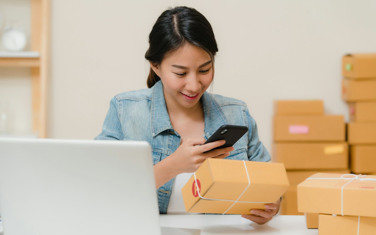 Persona preparando pedidos con cajas, un teléfono y un portátil