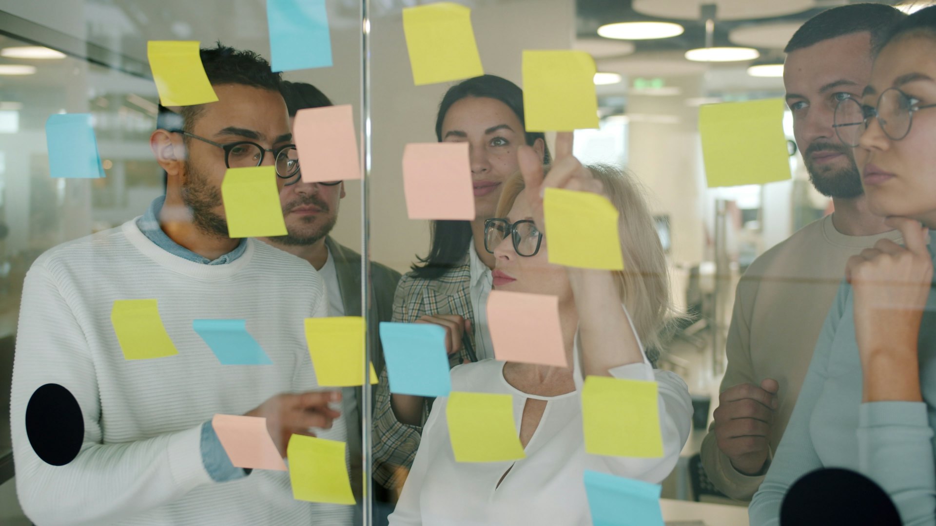 Equipo en una sesión de ideas con notas adhesivas sobre una pared de cristal